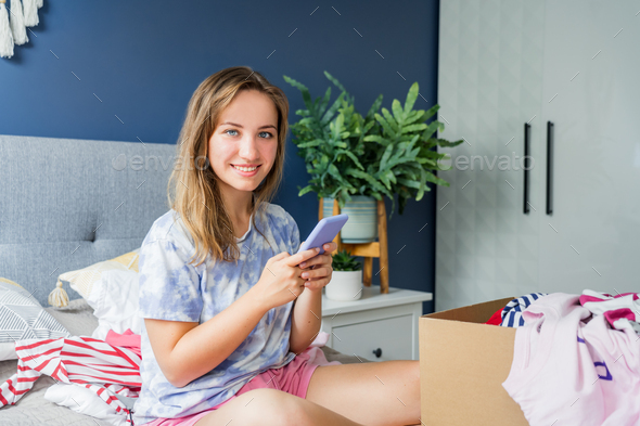 Smiling woman using smartphone to find places where to donate or sale clothes. Decluttering