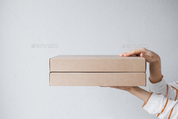 women\'s hands hold cardboard boxes on a gray background. food and drink delivery. biodegradable