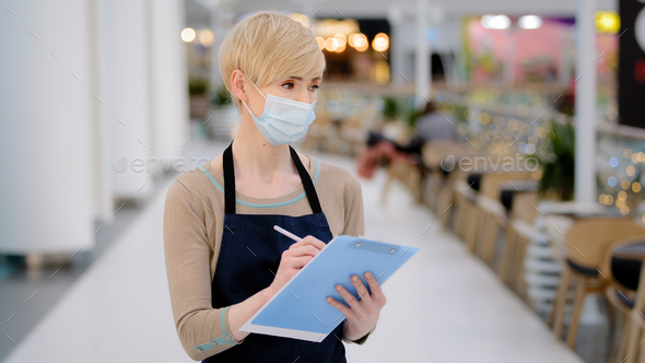 Close-up caucasian middle-aged woman cafeteria restaurant worker waitress in medic face mask writing