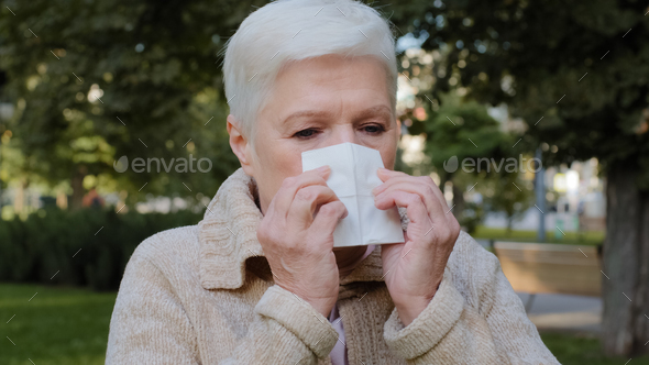 Allergic middle-aged lady feels unwell having flu symptom, ill old mature woman hold tissue sneezing