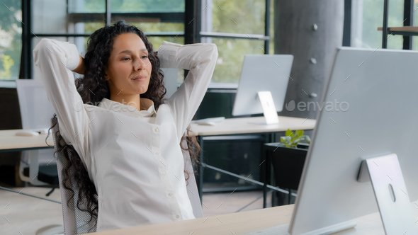 Relaxed contented young woman sitting at workplace enjoying finished work happy calm businesswoman