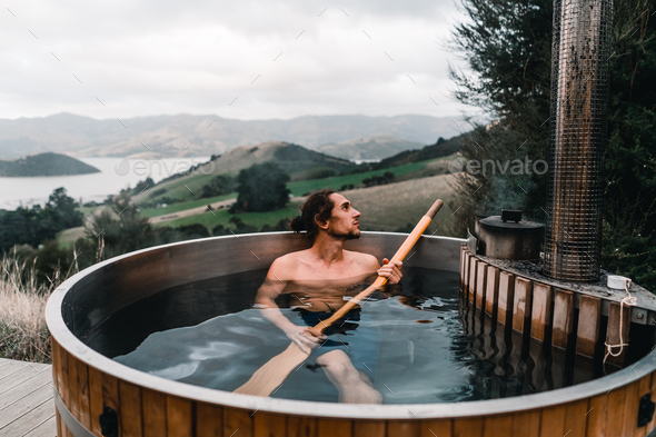 calm caucasian boy without clothes taking a bath with a long wooden spade in his hands inside a