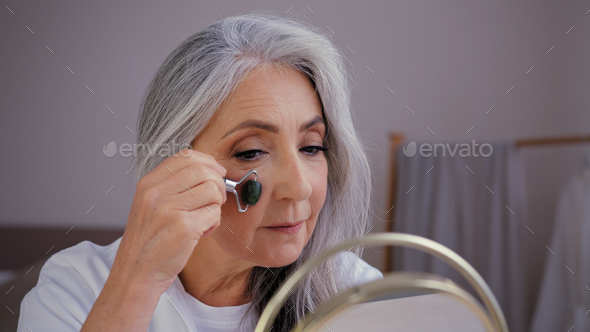 Close-up old gray-haired Caucasian woman model grandma elderly lady looking in mirror smooth out