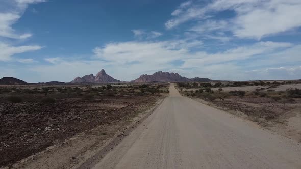 Drone footage of a long road in the desert with huge Erongo mountains alt