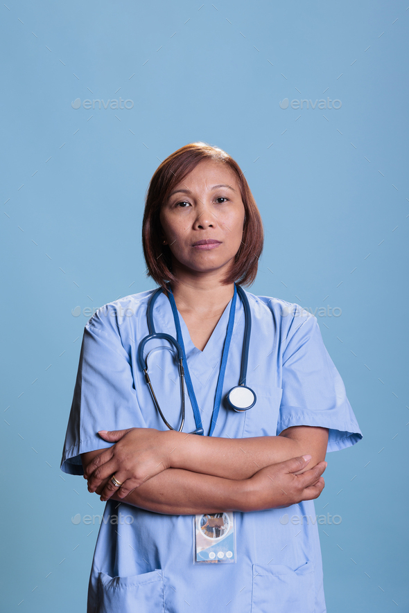 Elderly physician assistant with stethoscope standing with arm crossed in studio