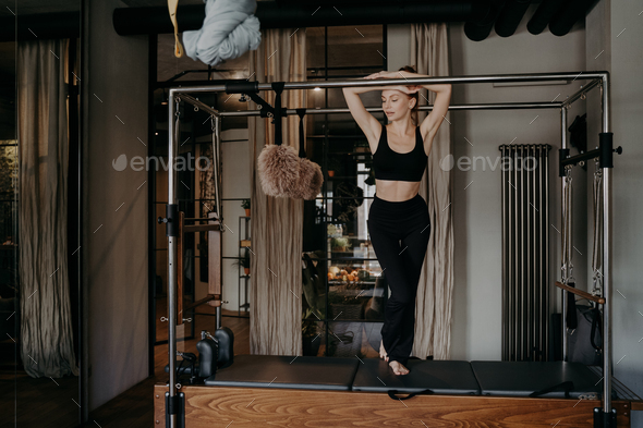 Young slim caucasian female resting on bar of pilates cadillac reformer  Stock Photo by StudioVK