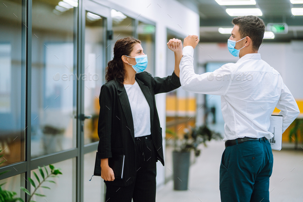 Portrait of two colleagues wearing face masks bumping elbows while ...