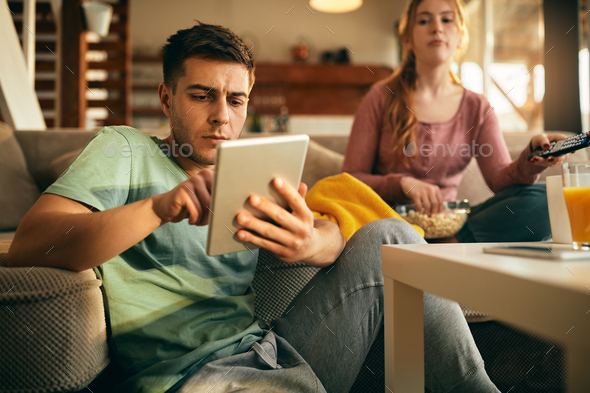 Young man surfing the net on touchpad while relaxing with his girlfriend at home. - Stock Photo - Images