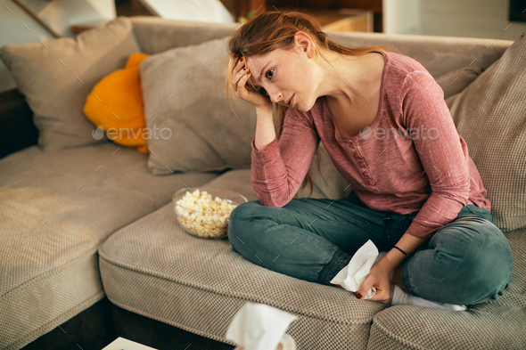 Young woman watching sad movie on TV at home.