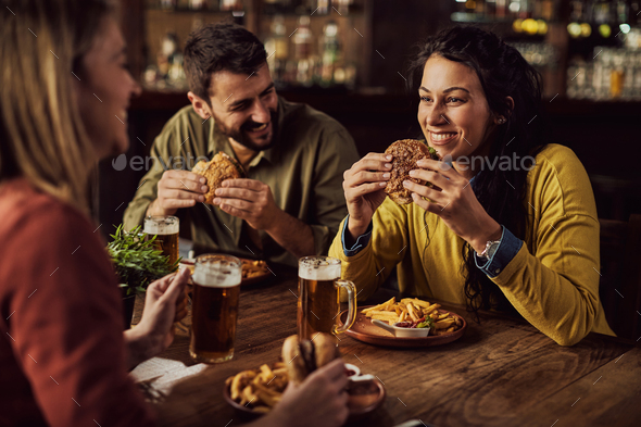 Young happy woman eating hamburgers with her friends in a pub.