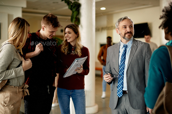 Mature university professor talking to his students in a hallway.