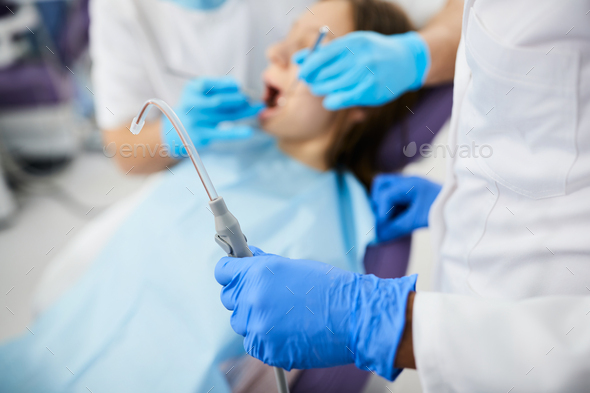 Close-up of dentist using dental suction tube during appointment with patient at dentist\'s office.