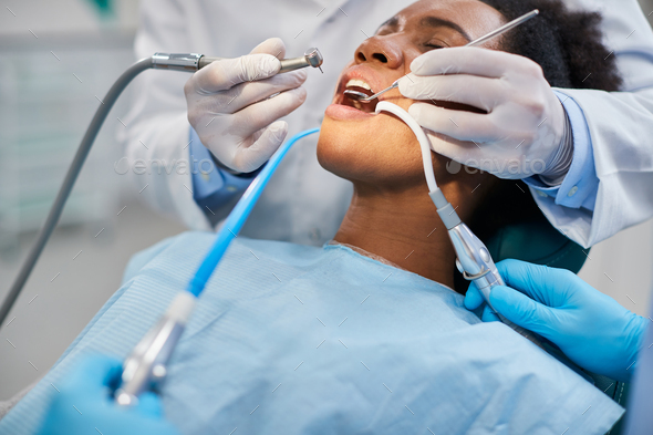 Black woman having dental drill procedure during teeth treatment at dentist\'s office.