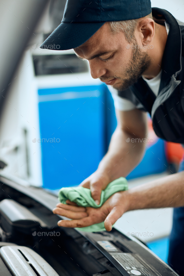 Young repairman wiping his hands after working on car engine in a workshop.