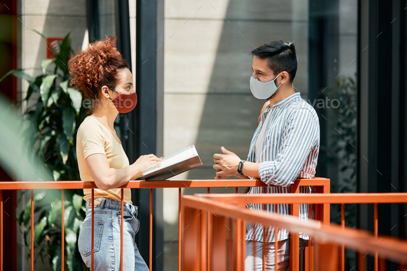 Two happy college students communicating while wearing face mask due to coronavirus pandemic.