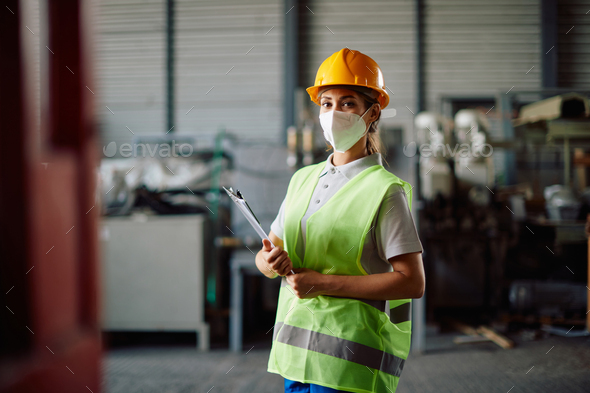 Portrait of female warehouse worker wearing face mask and storage compartment and looking at camera.