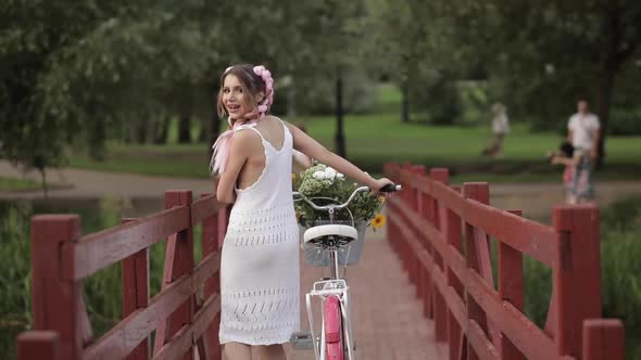 Romantic Sexy Girl in White Summer Dress Walking with Bicycle on Wooden Bridge at Forest Park