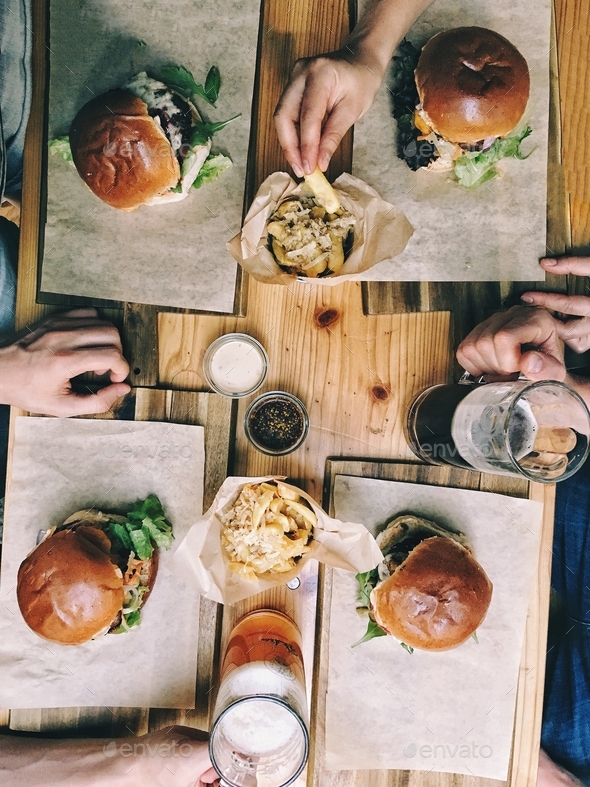 Top view of a group of friends eating burgers and fries with beer