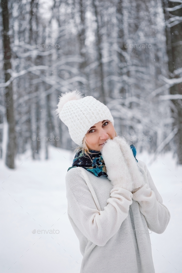 A young caucasian woman in winter forest. Snowy day walking. Hat, sweater, mittens outfit.