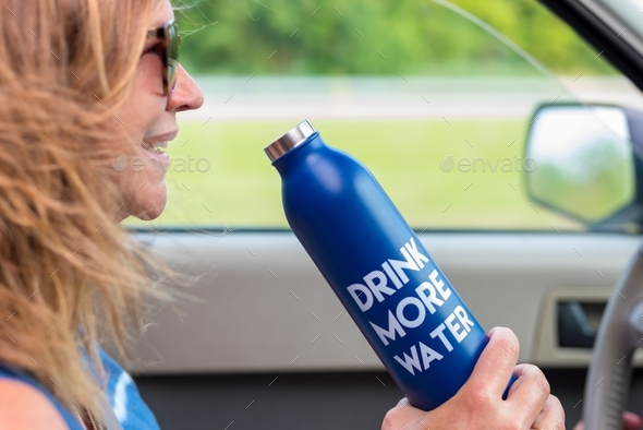 Smiling woman with water bottle driving a car, hair blowing in wind Stock  Photo by krisprahl