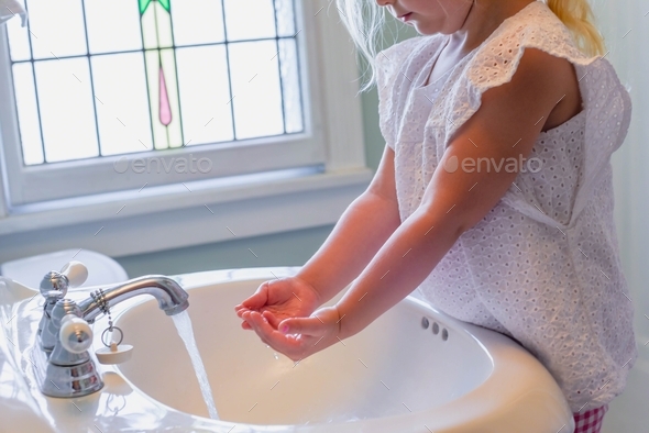 Little girl standing on step stool washing hands at the bathroom sink