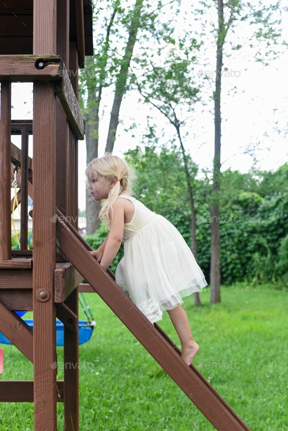 Cute little barefoot girl climbing play set ladder in the backyard