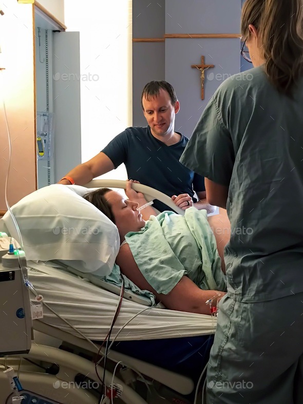 Woman rests between contractions while husband looks on in a hospital delivery room