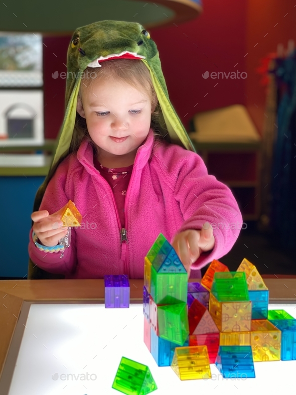 Toddler girl dressed up in a Dinosaur costume playing with blocks
