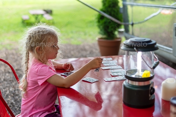 Little girl playing solitaire on a red outdoor table at a campsite - Stock Photo - Images