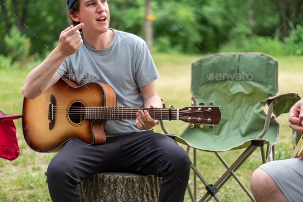 Candid portrait of a young guy playing guitar at a campsite