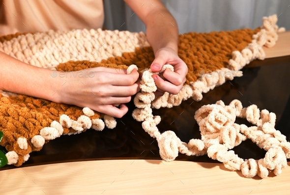 Women's hands knit plush yarn with camel-colored and ivory loops ...