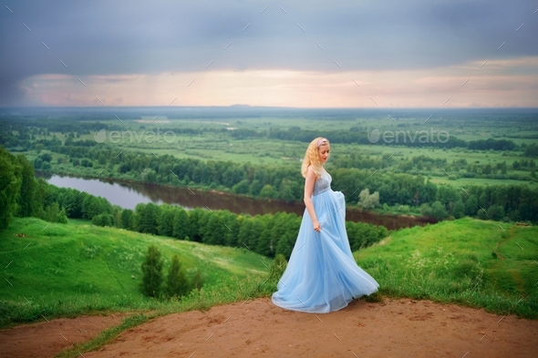A girl in a blue dress against the backdrop of a picturesque landscape on the mountain.