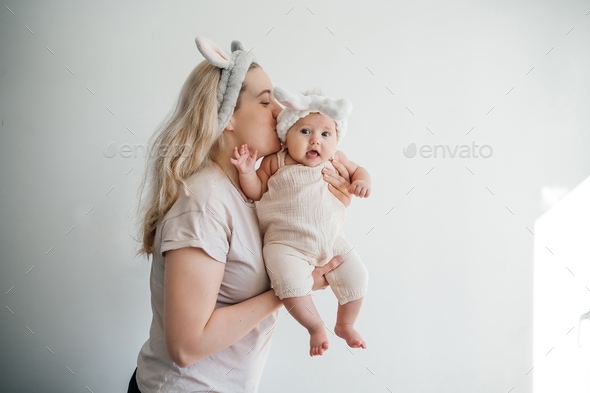 mom blonde and newborn daughter in white with rabbit ears photo on a light background celebrate East