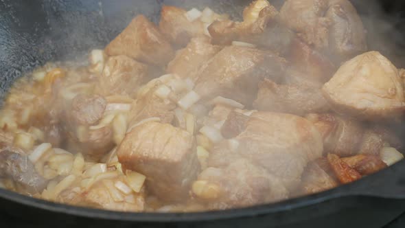 Cooking Process, Frying Pork Meat and Onion in Large Cauldron on Open Fire. 