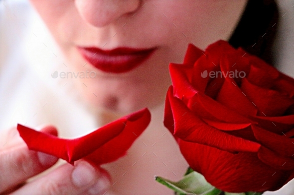 Minimalist image of women with red lips holding a red rose and rose petal close to face