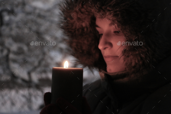Side view portrait of illuminated young woman wearing fur trimmed parka holding lighted candle.