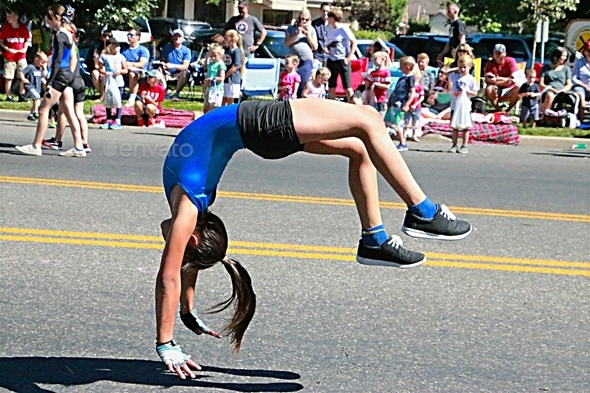 Young female acrobat doing flips down the street during a parade.