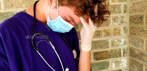 Young adult male ER Emergency Medical Technician looking stressed outside a hospital during pandemic