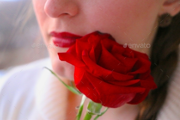 Minimalist image of female wearing red lipstick holding a red rose close to her face.