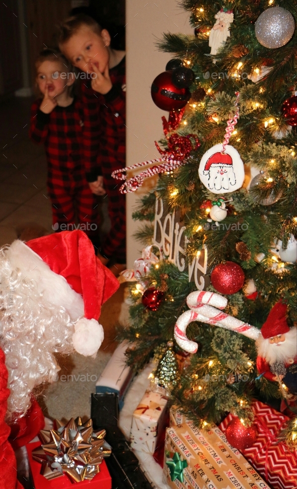 Vertical image of two children catching Santa leaving presents under ...