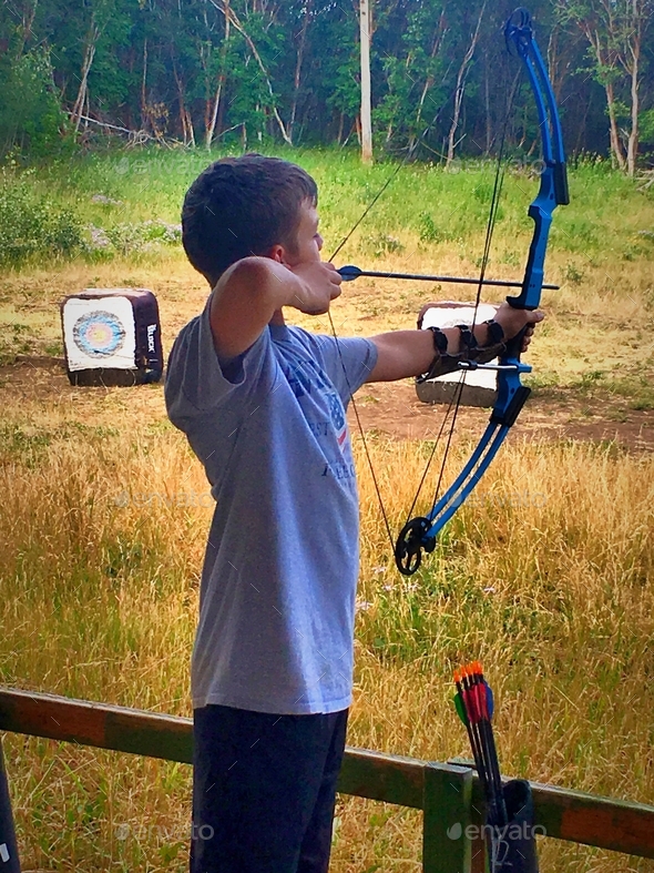Young archer taking aim at target during lesson at scenic outdoor archery range.