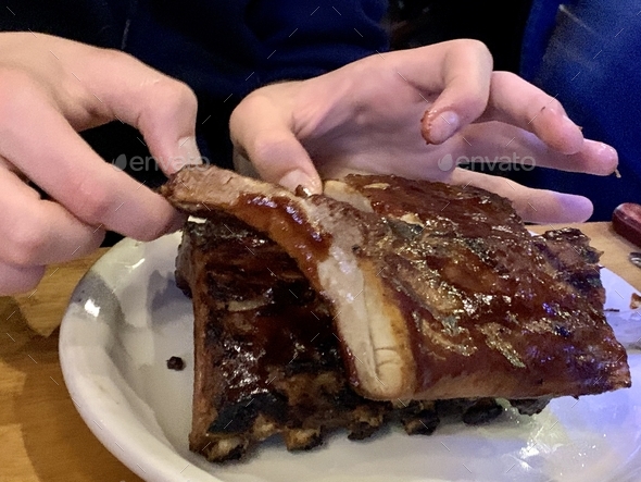 Hands digging in to a tender rack of slow cooked ribs in tangy sauce ...