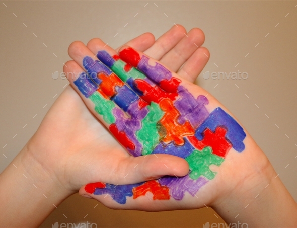 Autism Awareness: Human hands connected together with Autism puzzle pieces drawn on palm of hand.