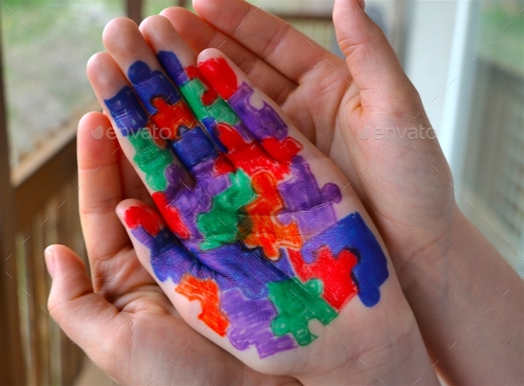 Mother holding hand of child with Autism puzzle pieces colored on palm of child\'s hand.