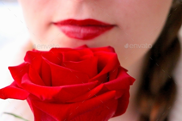 Minimalist style portrait of woman with red lips holding single long stemmed red rose.
