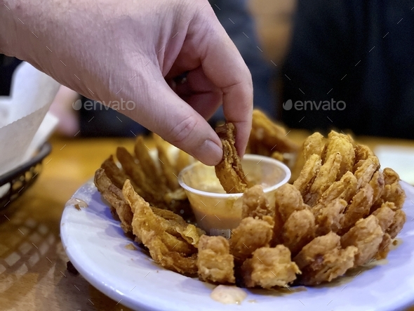 Hand dipping onion in sauce, restaurant appetizer. Dining out. Casual dining.