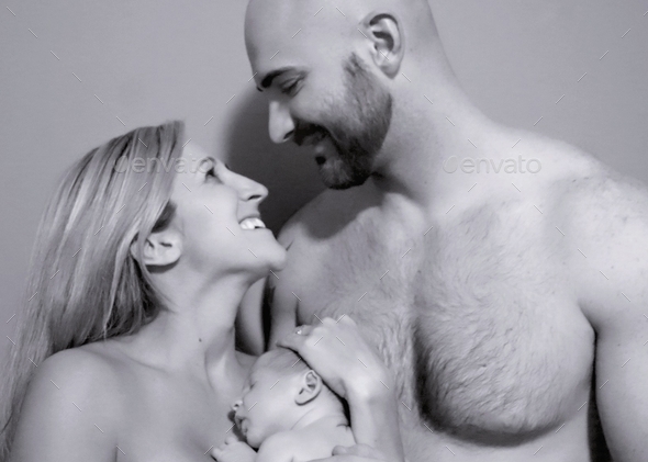 Monochromatic portrait of happy parents having skin-to-skin contact with newborn son.