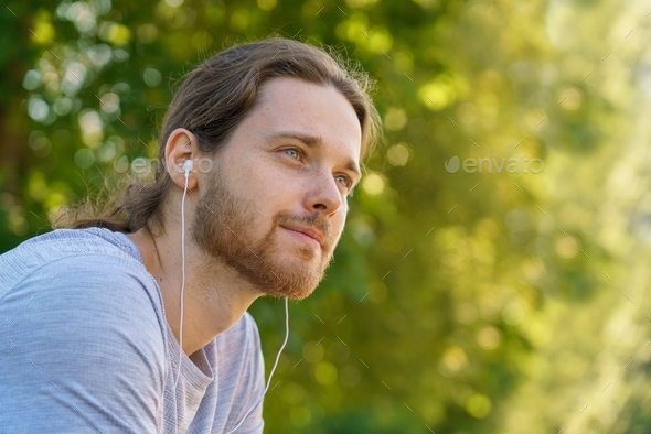 Young handsome bearded man in earphones resting after morning sport training