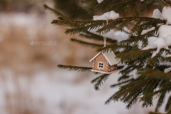 Christmas tree toy wooden house on a snow-covered Christmas tree. MINIMALIST HOLIDAY SEASON