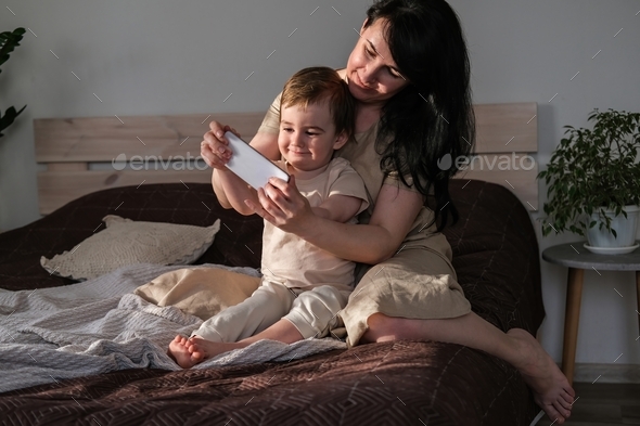 Mom and child play video games on smartphone while sitting on bed